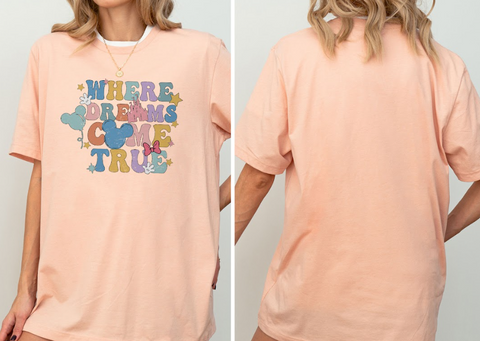 A woman wearing a peach-colored t-shirt with a colorful graphic and text on it.