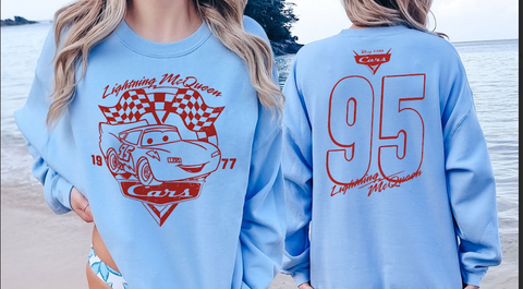 A woman wearing a light blue sweatshirt with a red and white design featuring a car and the text "Lightning McQueen" and "Cars" printed on it.