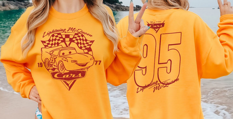 A person wearing a yellow sweatshirt with a graphic of Lightning McQueen from the Cars movie, along with the number 95.
