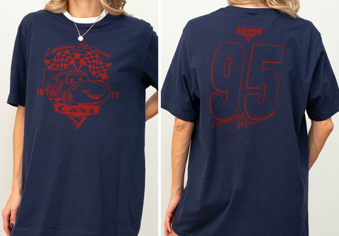 A navy blue t-shirt with a red graphic design on the front and back. The front design features a red car with the text "Lightning McQueen" and "Cars" written on it, along with the year "1977". The back design shows the number "95" and the text "Lightning McQueen" above it.