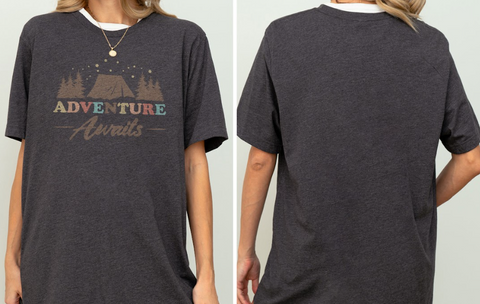 a person wearing a gray t-shirt with a graphic design featuring a tent and stars. The t-shirt has the text "Adventure Awaits" printed on it.