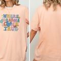 A woman wearing a peach-colored t-shirt with a colorful graphic and text on it.