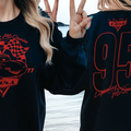 A person wearing a black sweatshirt with a red and black design featuring a car and the text "Lightning McQueen" and the number "95".