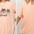 A woman wearing a peach-colored t-shirt with the text "Adventure Awaits" printed on it.