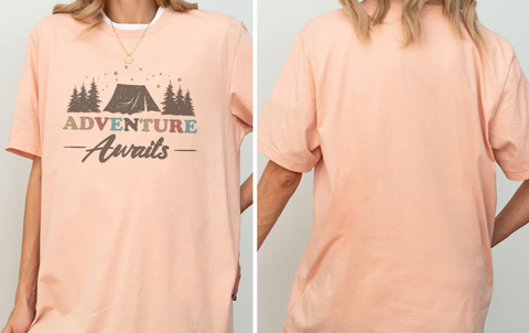 A woman wearing a peach-colored t-shirt with the text "Adventure Awaits" printed on it.