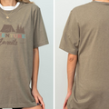 A woman wearing a gray t-shirt with the text "Adventure Awaits" printed on it.