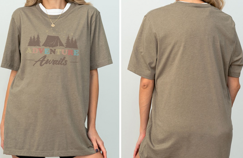 A woman wearing a gray t-shirt with the text "Adventure Awaits" printed on it.