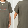 a person wearing a gray t-shirt with a graphic design featuring a mountain landscape and the text "ADVENTURE" printed on it.