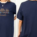 a person wearing a navy blue t-shirt with a graphic design featuring a tent and stars, along with the text "Adventure Awaits".