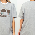 A gray t-shirt with a graphic design that says "Adventure Awaits" and features a tent and trees.