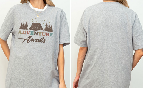 A gray t-shirt with a graphic design that says "Adventure Awaits" and features a tent and trees.