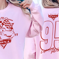 A person wearing a pink sweatshirt with a red and white design featuring a car and the text "Lightning McQueen" and "77" printed on it.