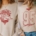 A woman wearing a white sweatshirt with a red and white design featuring a car and the text "Lightning McQueen" and "77 Cars".