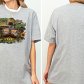 A gray t-shirt with a graphic design featuring a sombrero, cactus, and sunflower, along with the text "Cerveza y la Paz".