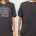 a person wearing a gray t-shirt with a colorful graphic design on it. The design features the text "WHERE DREAMS COME TRUE" along with various Disney-themed elements such as Mickey Mouse and stars.