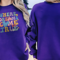 A woman wearing a purple sweatshirt with the text "WHERE DREAMS COME TRUE" printed on it, standing on a beach.
