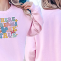 A woman wearing a pink sweatshirt with the text "WHERE DREAMS COME TRUE" printed on it, standing near the ocean.