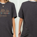 a person wearing a gray t-shirt with a graphic design featuring a tent and stars. The t-shirt has the text "Adventure Awaits" printed on it.