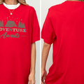 A red t-shirt with the text "ADVENTURE Awaits" printed on it, along with a graphic of a tent and trees.