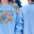 A woman wearing a blue sweatshirt with the text "WHERE DREAMS COME TRUE" printed on it, standing on a beach.