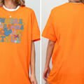 a person wearing an orange t-shirt with a colorful graphic and text on it.