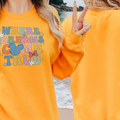 A woman wearing a bright yellow sweatshirt with the text "WHERE DREAMS COME TRUE" printed on it, standing on a beach with the ocean in the background.
