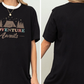 a person wearing a black t-shirt with a graphic design featuring a tent and the text "Adventure Awaits".